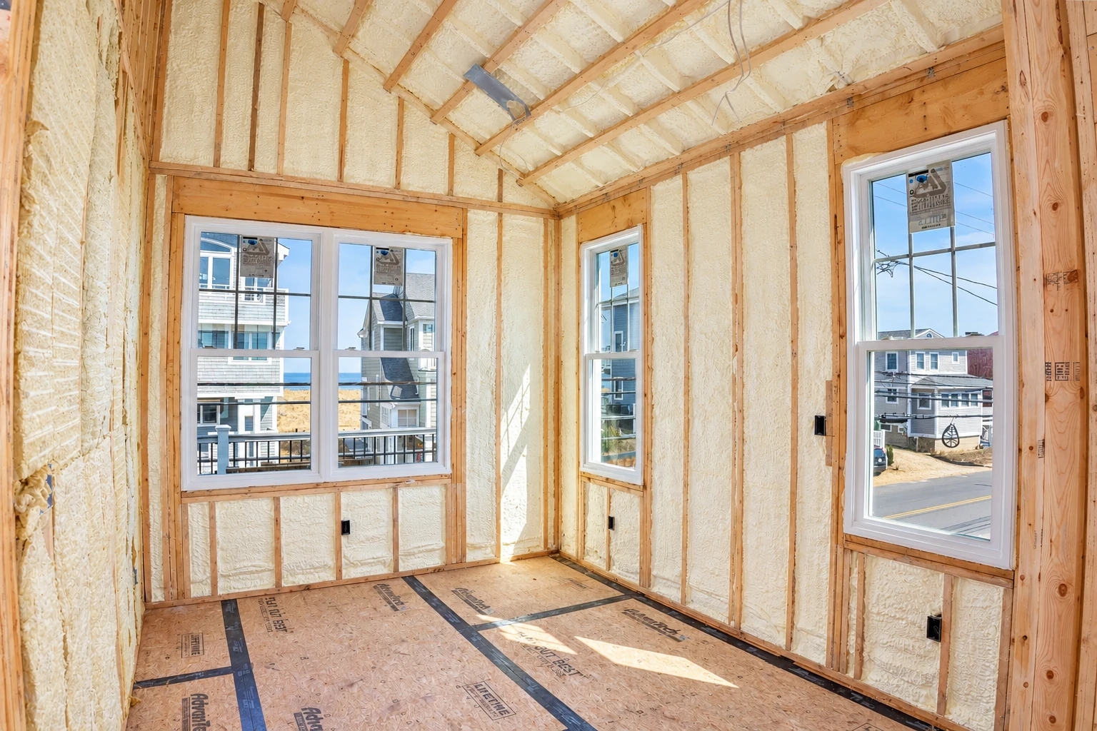 Unfinished room with pale spray foam filling the wall and roof framing around several windows.