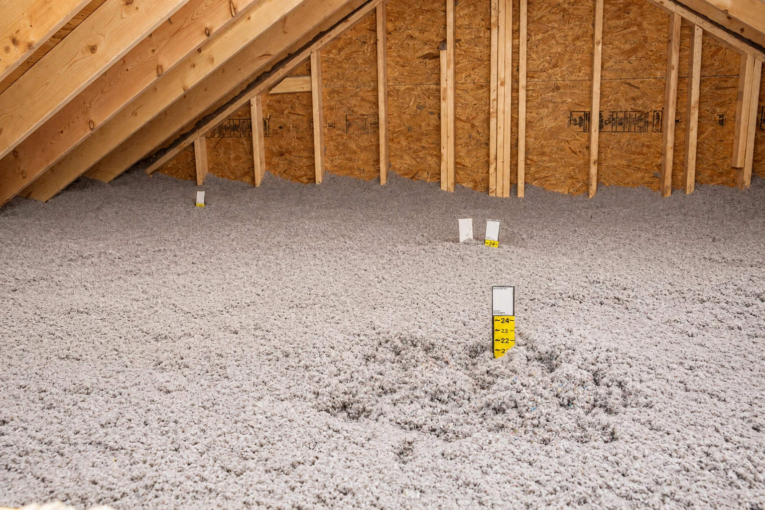 A thick layer of loose-fill insulation covers an attic floor beneath exposed roof trusses.