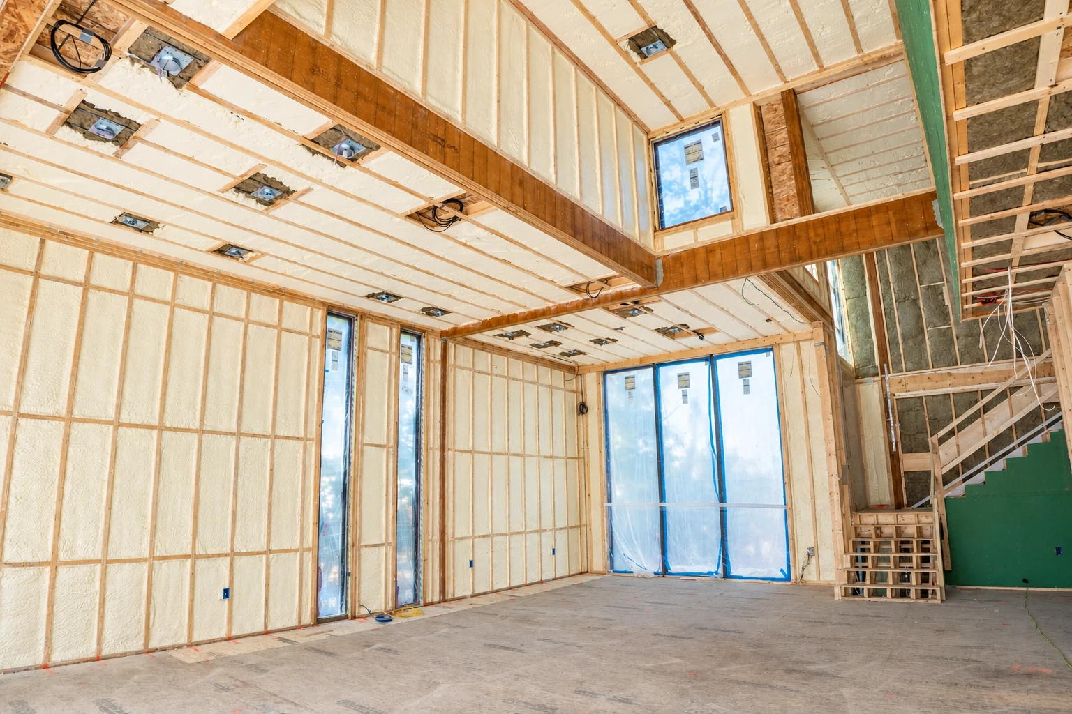 Unfinished home interior with white spray foam insulation filling wall and ceiling cavities around exposed framing.